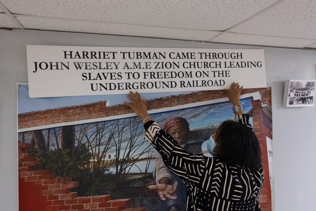 Dr. Norma Thomas holds up a sign above a printed mural featuring American abolitionist Harriet Tubman. Thomas hopes to secure funding for renovations to the church so that she can permanently install her Black history museum in its basement. Photo: Justin Hayhurst/100 Days in Appalachia